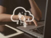 A cloud represented in the middle of the image representing cloud hosting. A person and a laptop.