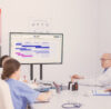 Pharma and healthcare. 4 people from the medical industry sitting at a meeting table looking at a screen with a board opened. They use a secure collaboration tool