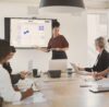 5 People from enterprise sector in a meeting room looking at a big screen with Conceptboard on it
